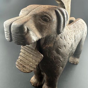 May include: A cast iron dog-shaped nutcracker with a textured, aged appearance. The dog's head opens to crack nuts, and the design includes a lever with the patent number 40273. The dog is brown and has a detailed, textured surface.
