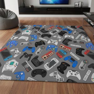 Peut inclure: Un tapis rectangulaire orné d'un motif répétitif représentant diverses manettes de jeu vidéo et consoles portables dans des tons de bleu, rouge, noir, blanc et gris sur un fond gris uni, illustrant divers modèles de matériel de jeu.