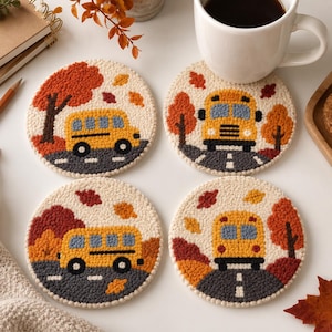 Könnte beinhalten: Ein Set aus vier runden Punch-Needle-Untersetzern mit einem gelben Schulbus auf einer grauen Straße. Das Design zeigt herbstliche Bäume mit orangefarbenen und roten Blättern sowie verstreutes Herbstlaub auf einem cremeweißen Hintergrund.