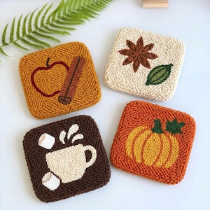Könnte beinhalten: Vier quadratische Punch-Needle-Untersetzer mit saisonalen Motiven. Ein senfgelber Untersetzer zeigt einen Apfel und eine Zimtstange, ein cremefarbener einen Sternanis und ein Blatt, ein brauner eine Tasse mit Marshmallows und ein orangefarbener einen Kürbis.