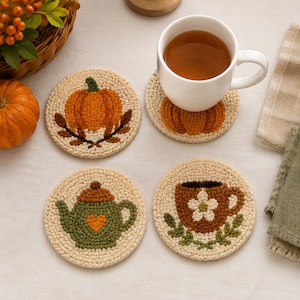 Puede incluir: Cuatro posavasos redondos de ganchillo color crema con diseños texturizados: una calabaza naranja con hojas marrones, una tetera verde con un corazón naranja, una taza marrón con una flor blanca y un diseño de calabaza bajo una taza blanca.