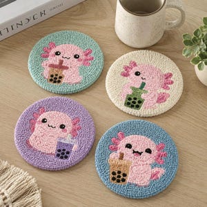 May include: Four circular punch needle coasters featuring pink axolotls holding boba tea drinks. The coasters are colored light blue, cream, purple, and medium blue, each showcasing a unique axolotl character with a different colored boba cup.