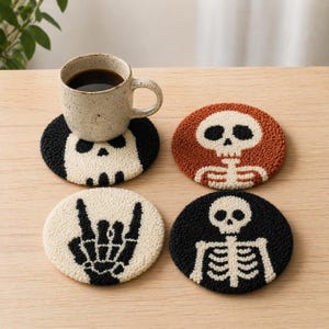 Könnte beinhalten: Set mit vier Untersetzern zum Thema Halloween. Jeder Untersetzer hat ein anderes Design: einen Schädel, ein Skelett, eine Hand, die eine Rock'n'Roll-Geste macht, und ein Skelett. Die Untersetzer sind schwarz, weiß und orange.
