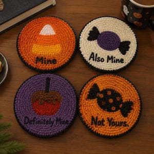May include: Four round, crocheted coasters featuring Halloween-themed designs. One orange coaster shows a candy corn with the text Mine. One cream coaster shows a purple candy with the text Also Mine. One purple coaster shows a candy apple with the text Definitely Mine. One orange coaster shows a black candy with the text Not Yours.