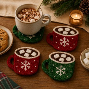 Puede incluir: Un juego de tres posavasos de ganchillo con forma de tazas llenas de chocolate caliente, nubes y copos de nieve blancos. Dos posavasos son rojos y uno es verde, cada uno con una parte superior marrón y cuadrados blancos.