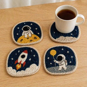 May include: Set of four handmade crochet coasters with space-themed designs. Each coaster features a dark blue background with an astronaut, rocket, or moon. The coasters have a beige border and are perfect for protecting surfaces.