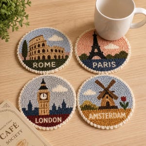 May include: Four round crochet coasters featuring embroidered landmarks: the Colosseum labeled ROME, the Eiffel Tower labeled PARIS, Big Ben labeled LONDON, and a windmill labeled AMSTERDAM. Each coaster has a cream-colored border.