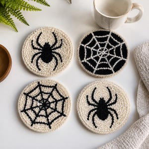 May include: A set of four round crochet coasters featuring two designs: a black spider on a cream background and a black spiderweb on a cream background. The coasters are crafted with textured yarn, displaying clear, contrasting black and cream patterns.