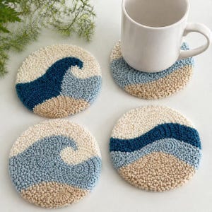 Peut inclure: Ensemble de quatre dessous de verre ronds avec un motif de vagues. Chaque dessous de verre présente un motif texturé et touffeté dans des tons crème, bleu et beige. Un dessous de verre est surmonté d'une tasse blanche. Les dessous de verre mesurent environ 10 cm de diamètre.