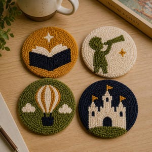 Op de afbeelding: Vier ronde punch needle onderzetters met verschillende ontwerpen: een mosterdgele onderzetter met een open boek, een crèmekleurige met een groen figuur met een telescoop, een groene met een heteluchtballon en een marineblauwe met een wit kasteel.