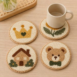 Puede incluir: Cuatro posavasos redondos de ganchillo en color crema con diseños distintos: una corona amarilla con un corazón verde, una flor amarilla con hojas verdes, una casa marrón con arbustos verdes y una cara de oso de peluche con pajarita verde.