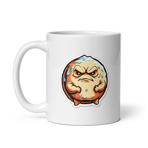 May include: White ceramic mug featuring a cartoon illustration of an angry, orange, round creature with a stern expression. The creature has a white patch on its head and is surrounded by blue accents. The mug has a curved handle.