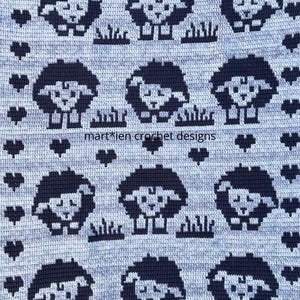 Op de afbeelding: Een gehaakte deken met een herhalend patroon van zwarte schapen, gras en hartvormen op een lichtgrijze achtergrond. De tekst "mart*ien crochet designs" is zichtbaar.
