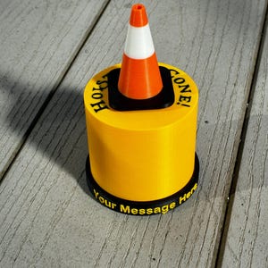 May include: A yellow cylindrical object with a black base and top, featuring a miniature orange and white traffic cone. The text "Hole Gone!" is printed on the top, and "Your Message Here" is on the base.
