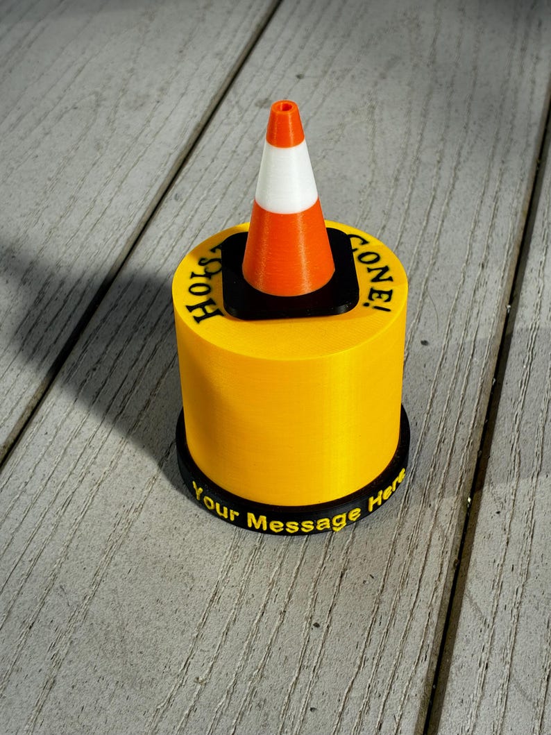 May include: A yellow cylindrical object with a black base and top, featuring a miniature orange and white traffic cone. The text "Hole Gone!" is printed on the top, and "Your Message Here" is on the base.