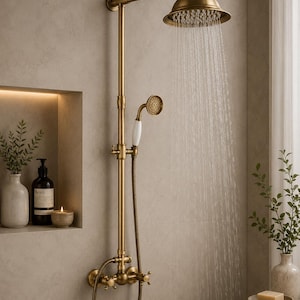 May include: A wall-mounted shower system in a brushed brass finish featuring a large round rainfall showerhead, a handheld shower attachment with a white handle, and two cross-style control knobs. Water flows from the main showerhead.