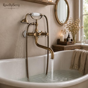 May include: A wall-mounted antique brass bathtub faucet set with a handheld shower attachment. The fixture features white ceramic accents with floral patterns on the handles and shower head. Water flows from both the main spout and the shower head.