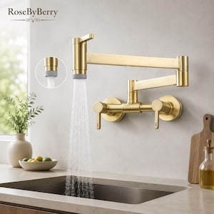 Può includere: Un rubinetto a parete per riempire pentole in oro spazzolato con un braccio articolato doppio e due maniglie a leva. L'acqua scorre dall'aeratore in un lavandino. Il marchio RoseByBerry è stampato nell'angolo in alto a sinistra.