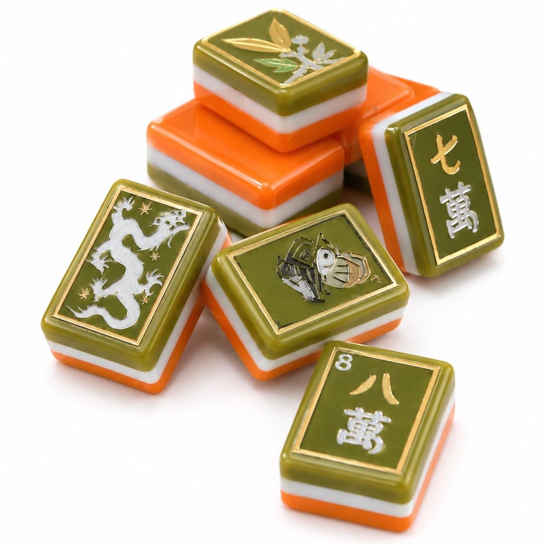 May include: A collection of six mahjong tiles featuring a three-layer design with an olive green top, a white middle, and an orange base. The tiles display various engraved symbols including a white dragon, a plant, and Chinese characters.