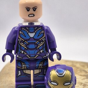 Peut inclure: Une figurine Lego violette et bleue avec un casque assorti. La figurine a un teint clair et une expression sérieuse. L'armure présente des détails bleus et dorés. Le casque est orné d'une plaque faciale dorée et d'éléments bleus.