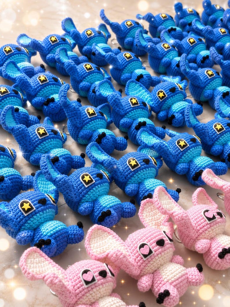 May include: Crocheted blue and pink character plushies with black accents and star-shaped details. The blue plushies have a yellow star on their heads, while the pink ones have heart-shaped details. The plushies are arranged in rows.
