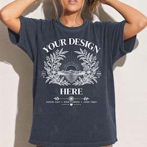 May include: A charcoal grey short-sleeve t-shirt featuring a white graphic print. The design includes the text "YOUR DESIGN HERE" surrounding a landscape illustration of mountains, a sun, and floral wreaths, with "EST. 2026" and "NATURE DAYS WILD FLOWERS GOOD VIBES".