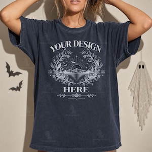 Może przedstawiać: Ciemnoszary t-shirt z krótkim rękawem z białym nadrukiem graficznym z napisem "YOUR DESIGN HERE". Wzór przedstawia górski krajobraz, dynie, nietoperze i gałęzie. Koszulka ma okrągły dekolt i luźny, swobodny krój.