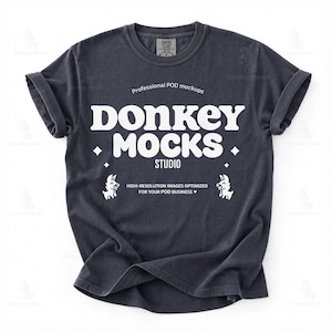 May include: A dark charcoal gray short-sleeve t-shirt featuring white text that reads "Professional POD mockups DONKEY MOCKS STUDIO" and "HIGH-RESOLUTION IMAGES OPTIMIZED FOR YOUR POD BUSINESS" with two small donkey illustrations and four-pointed stars.