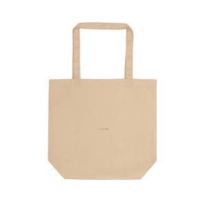 May include: A beige tote bag with two handles. The bag has a rectangular shape with a flat bottom and a small, unreadable text in the center. The handles are the same color as the bag.