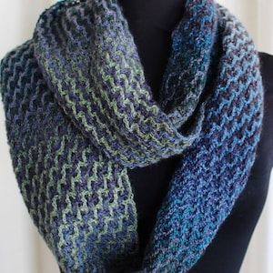 Könnte beinhalten: Ein blauer, grüner und schwarzer gestrickter Infinity-Schal mit Chevron-Muster.