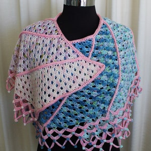 Pode incluir: Um xale de crochê em tons de rosa, azul e verde. O xale tem um delicado padrão de renda e é adornado com pequenas contas.