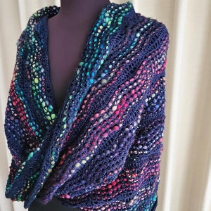 May include: A dark blue crochet shawl with a colorful, speckled pattern. The shawl is draped over a mannequin.