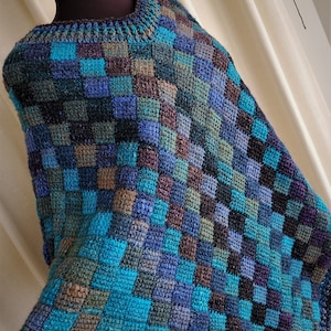 May include: A crocheted poncho with a checkered pattern in shades of blue, teal, brown, and black.