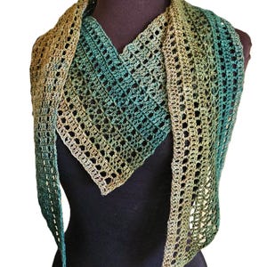 May include: A crocheted scarf with a gradient of green, brown, and beige colors. The scarf is displayed on a mannequin and has long, flowing ends.