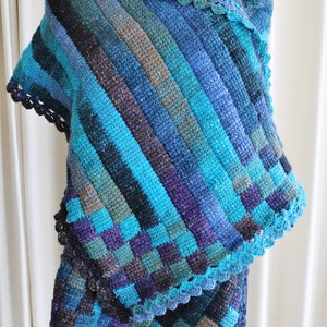 May include: A blue, green, and purple crocheted shawl with a crocheted border. The shawl is draped over a mannequin.