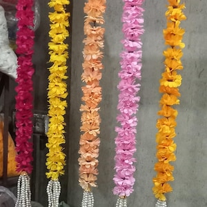 May include: A collection of colorful floral garlands in shades of red, yellow, orange, pink, and yellow-orange. Each garland is adorned with a beaded tassel at the bottom, creating a decorative and festive look. These garlands are suitable for various celebrations.