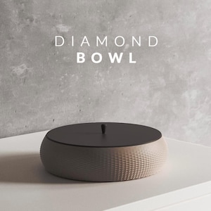 Peut inclure: Un bol rond avec un corps beige clair texturé et un couvercle gris foncé. Le couvercle a un petit bouton. Le corps du bol présente un motif géométrique. Le texte "DIAMOND BOWL" est affiché en blanc.