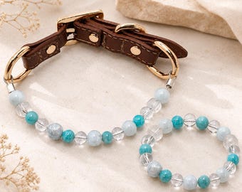 May include: A brown leather collar with gold-toned metal hardware and a matching beaded bracelet. Both items feature a repeating pattern of clear, light blue, and turquoise round beads strung together with metallic accents and connectors.