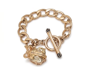 May include: Gold-tone chain bracelet with a heart-shaped charm. The charm features a light yellow gemstone and the words "Juicy Couture". The bracelet has a toggle clasp with black accents.