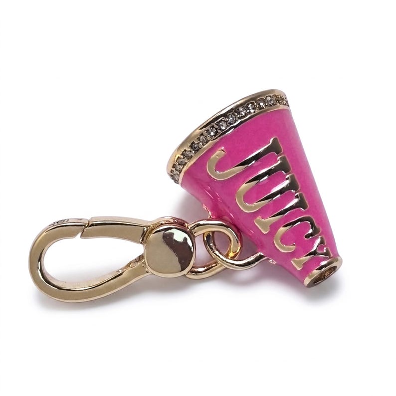 May include: A pink and gold charm in the shape of a megaphone. The word "Juicy" is written in gold lettering on the side of the megaphone. The megaphone has a gold rim with small, clear stones. A gold-colored clasp is attached.