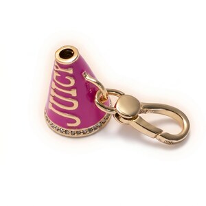 May include: A gold-toned metal charm in the shape of a cheerleader megaphone. The megaphone is magenta with the word "JUICY" in gold lettering. The base is encrusted with small, clear crystals, and it has a gold clasp.