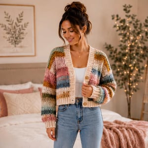 May include: A cropped, long-sleeved cardigan featuring a chunky crochet knit pattern with horizontal stripes in various colors including cream, pink, blue, and mustard yellow. The garment has a V-neckline, ribbed cuffs, and a front button closure.