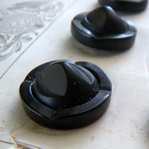 May include: Four black plastic buttons with a raised, pointed center. The buttons have a shiny, smooth finish.