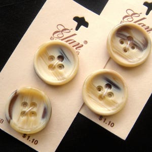 May include: Three beige buttons with brown and black swirl patterns and four holes. The buttons are on a white card with the text "Elam Buttons" and "$1.10".