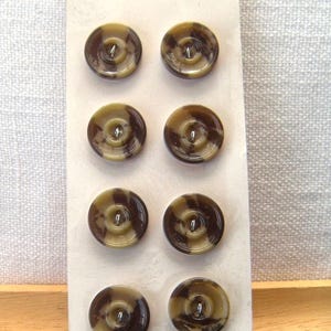 May include: Eight round buttons with a brown and tan swirl pattern are displayed on a white card. The card has the text "Buttons By chwanda" in a script font. The buttons are made of a glossy material and have a central hole for sewing.