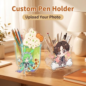 Puede incluir: Soportes para bolígrafos de acrílico transparente con diseños de personajes de dibujos animados. Uno presenta una bebida verde con un personaje, el otro un personaje sentado en un hueso. Se muestra el texto "Custom Pen Holder" y "Upload Your Photo".