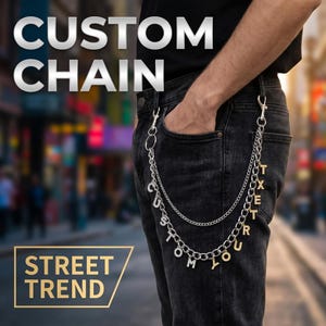 Könnte beinhalten: Eine silberfarbene Geldbörsenkette an einer schwarzen Jeans, bestehend aus zwei Lagen mit hängenden Buchstabenanhängern, die CUSTOM YOUR TEXT bilden. Der Text CUSTOM CHAIN und STREET TREND ist im Bild zu sehen.