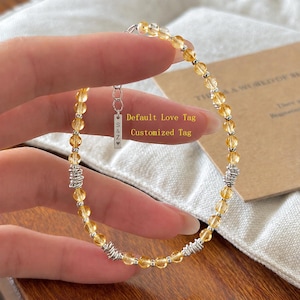Può includere: Un braccialetto di perline con pietre di citrino giallo traslucido alternate a piccole perline color argento e accenti in filo metallico color argento testurizzato. Un'etichetta rettangolare in metallo color argento reca l'incisione S&Z e un cuore.