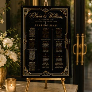 May include: A black rectangular seating plan sign with gold geometric borders and text. The sign displays the names Olivia & William, the date 20 September 2025, and a list of ten tables with guest names, all mounted on a gold metal tripod easel.