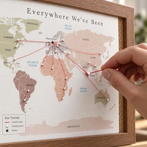 May include: A framed cork board map titled Everywhere We've Been, featuring a world map with white pins marking locations connected to Manchester by red thread. A legend at the bottom defines the travel route, visited places, and home location.